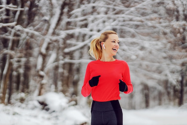 Glückliche fitte Sportlerin, die am verschneiten Wintertag im Wald joggt. Outdoor-Fitness, Winterfitness, gesunder Lebensstil