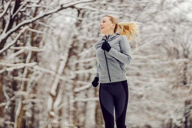 Glückliche fitte Sportlerin, die am verschneiten Wintertag in der Natur joggt. Gesundes Leben, Wintersport