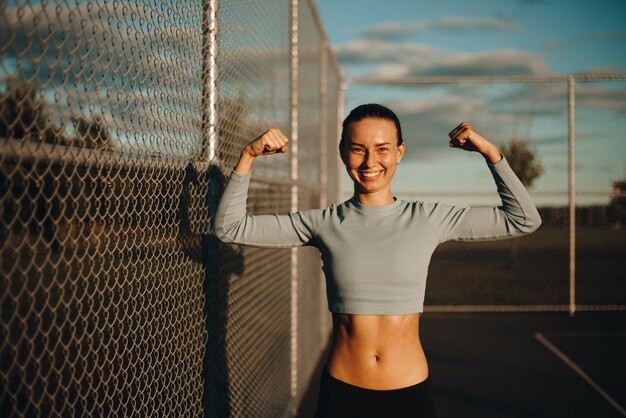 Glückliche Frau auf dem Basketballfeld. Eine junge Frau zeigt ihre Muskeln in ihren Armen. Porträtfoto.