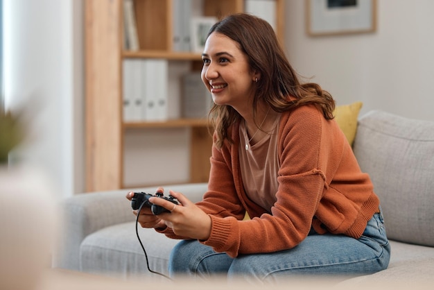 Glückliche Frau auf dem Sofa und beim Spielen von Videospielen zum Entspannen oder in der Freizeit im Wohnzimmer für Unterhaltung zu Hause. Weibliche Person lächelt mit Controller für Konsole oder Online-Gaming auf der Lounge-Couch im Haus