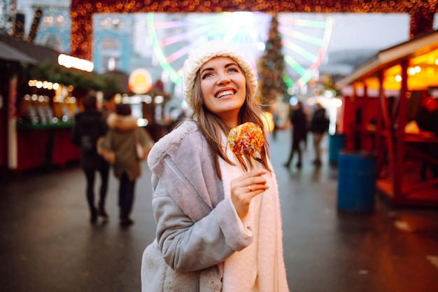 Glückliche Frau auf dem Weihnachtsmarkt mit karamellisiertem Apfel Outdoor-Aktivitäten zu Weihnachten