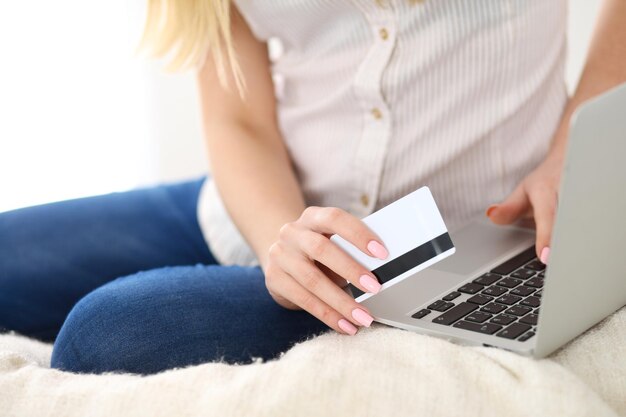 Glückliche Frau beim Online-Shopping zu Hause Nahaufnahme einer Hand, die eine Kreditkarte neben einem Laptop hält