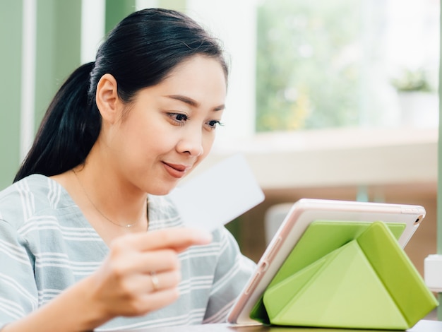 Glückliche frau benutzt eine weiße modellkreditkarte für das on-line-einkaufen auf tablette.