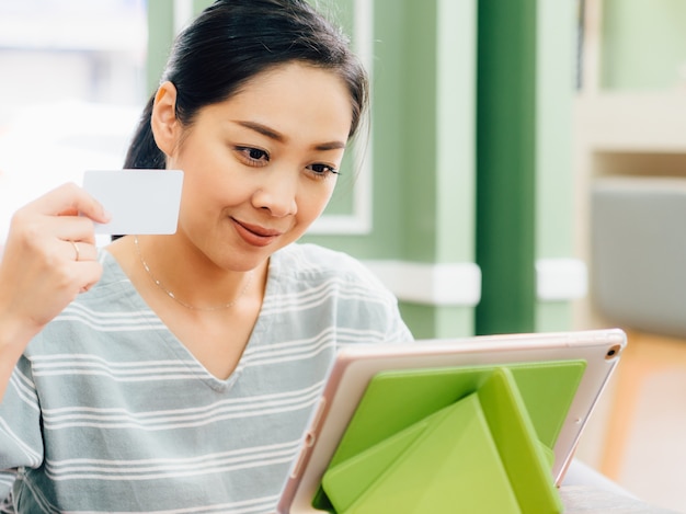 Glückliche Frau benutzt eine weiße Modellkreditkarte für das on-line-Einkaufen auf Tablette.