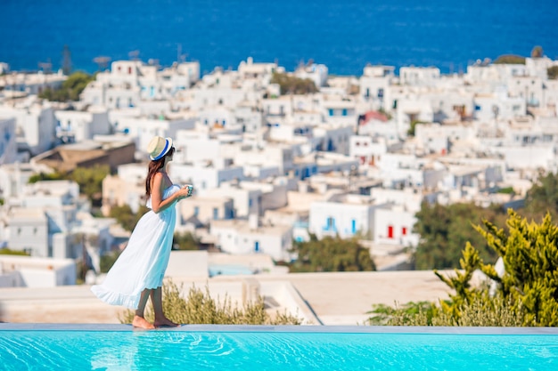 Glückliche Frau, die am Rand des Pools mit erstaunlicher Ansicht über Mykonos, Griechenland sich entspannt