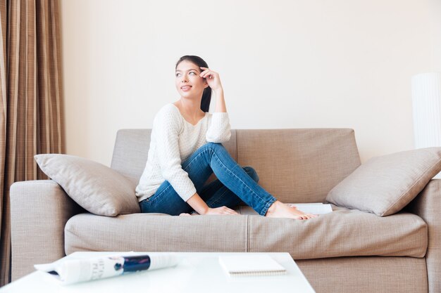 Glückliche Frau, die auf dem Sofa sitzt und zum Fenster wegschaut