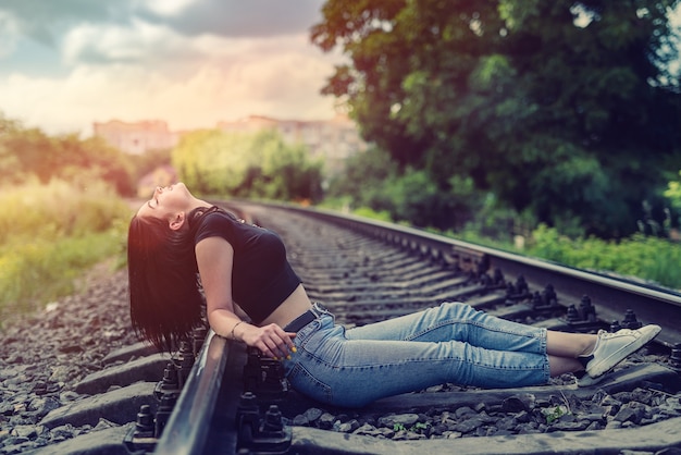 Glückliche Frau, die auf der Eisenbahn im Sommertuch, Eisenbahnschienen, Lebensstil sitzt