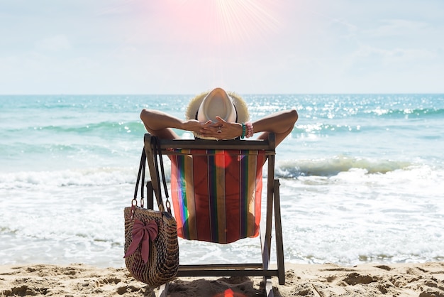 Foto glückliche frau, die auf einem klappstuhl am strand, entspannung auf dem tropischen strand sitzt. reise-konzept