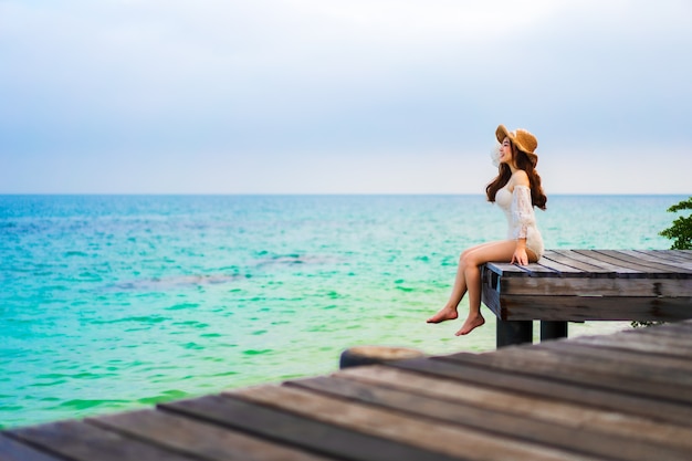 Glückliche Frau, die auf einer hölzernen Brücke im Meeresstrand auf Koh MunNork Island, Rayong, Thailand sitzt