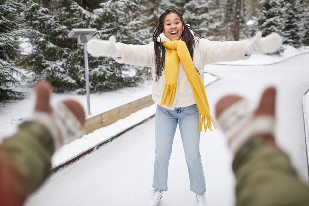 Glückliche Frau, die auf Eisbahn mit ihrem Freund Schlittschuh läuft, der sie fängt