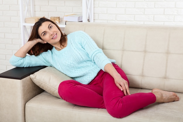 Glückliche Frau, die auf Sofa sitzt und zu Hause entspannt.