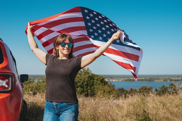 Glückliche Frau, die die USA-Flagge hält und den Sonnenuntergang in der Natur genießt Freier Lebensstil