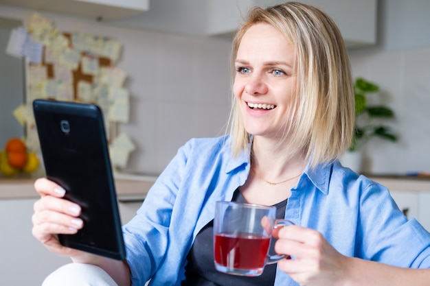 Glückliche Frau, die digitales Tablett für Videoanruffreunde und -eltern verwendet, lächelndes Mädchen, das zu Hause Küche Spaßgruß online durch Computer-Webcam sitzt, die Videoanruf macht