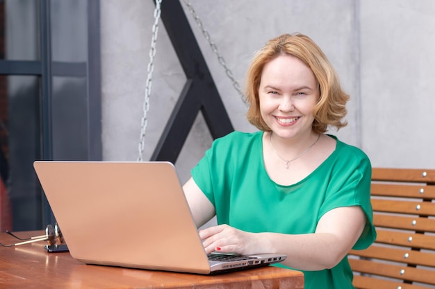 Glückliche Frau, die eine Anwendung auf einem digitalen Laptop in einem Straßencafé verwendet