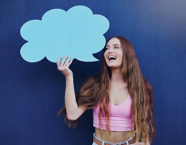 Glückliche Frau, die eine Sprechblase mit Mockup-Platz hält, die an einer blauen Wand mit einem Schild steht Gen z Happiness und junge Frau mit einem Chat-Board mit Mock-up oder Kopierraum für Marketing oder Werbung