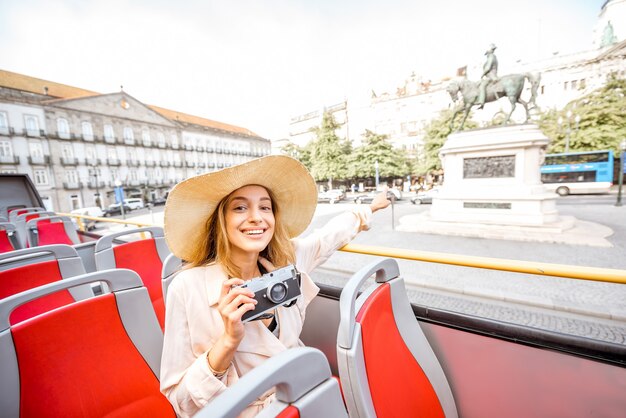 Glückliche Frau, die einen Ausflug mit dem offenen Touristenbus auf dem Freiheitsplatz in der Stadt Porto, Portugal, macht