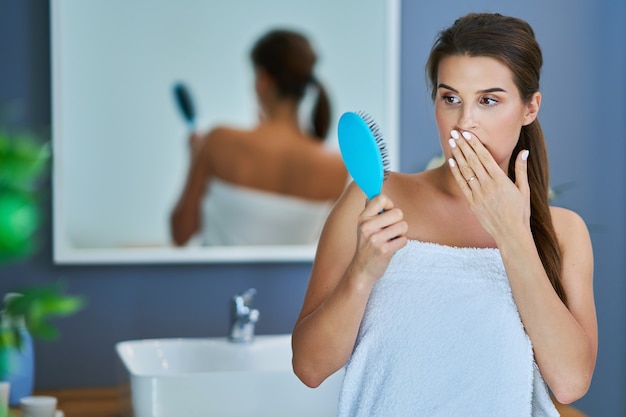 Glückliche Frau, die Haare im Badezimmer bürstet und Probleme mit Haarausfall hat