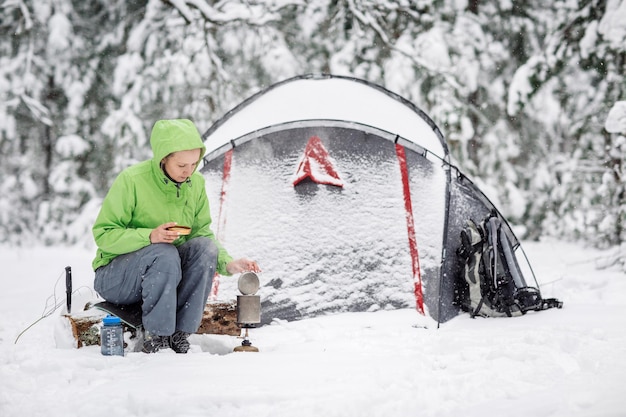 Glückliche Frau, die in der Nähe des Winterzeltlagers im Schneewald kocht