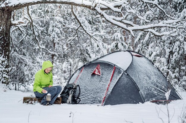 Glückliche Frau, die in der Nähe des Winterzeltlagers im Schneewald kocht