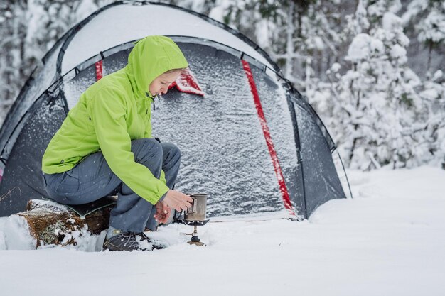 Glückliche Frau, die in der Nähe des Winterzeltlagers im Schneewald kocht