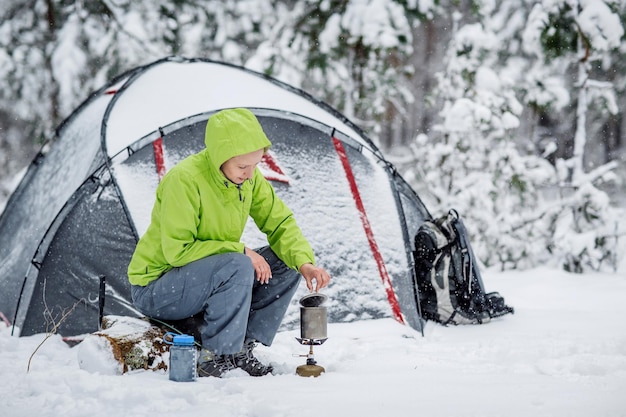 Glückliche Frau, die in der Nähe des Winterzeltlagers im Schneewald kocht