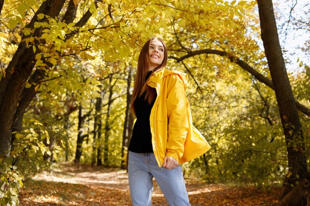 Glückliche Frau, die in gelber Kleidung vor den gelben Herbstblättern lacht. Lächeln Herbst