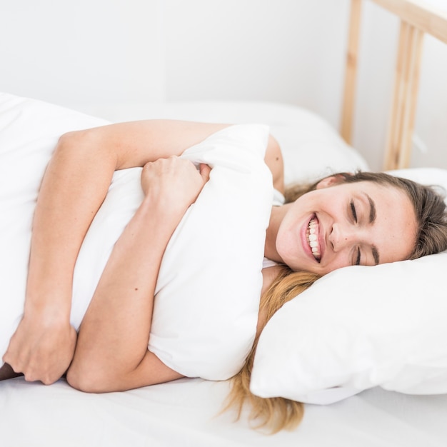 Glückliche Frau, die Kissen beim Lügen auf Bett umarmt