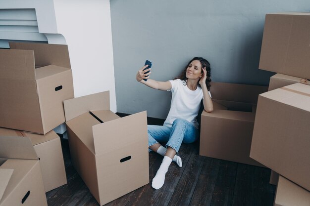 Glückliche Frau, die Kisten auspackt und Selfie in einer neuen luxuriösen Wohnung macht Erfolgskonzept