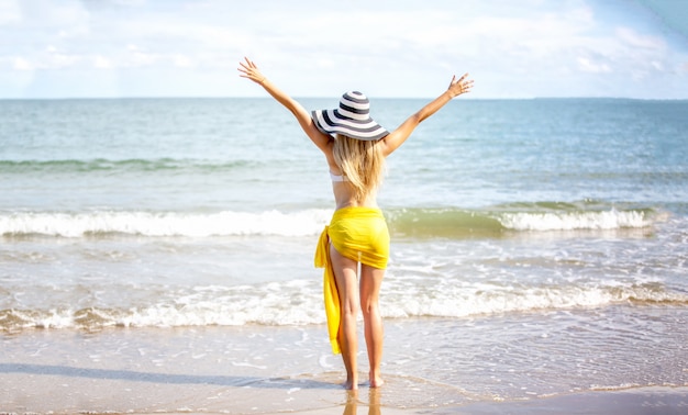 Glückliche Frau, die lächelt und Spaß am Strand hat. Sommerporträt des jungen schönen Mädchens am Strand mit gelbem Schal und Hut.