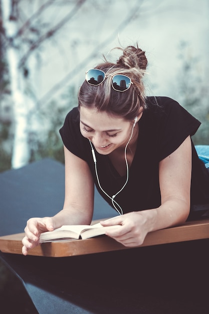 Glückliche Frau, die mit Kopfhörern Musik hört und ein Buch auf der Straße liest