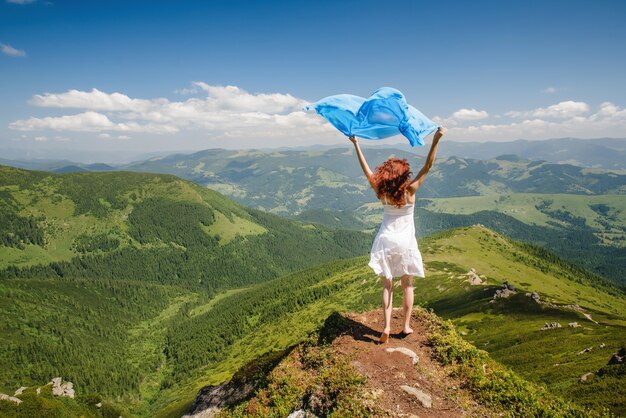 Glückliche Frau, die Natur in den Bergen genießt und blauen Schal in den Händen hält