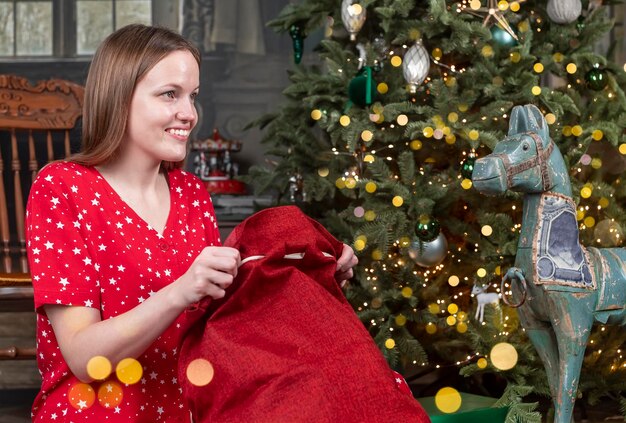 Glückliche Frau, die rote Weihnachtstasche von Santa in der Nähe von Weihnachtsbaum auspackt