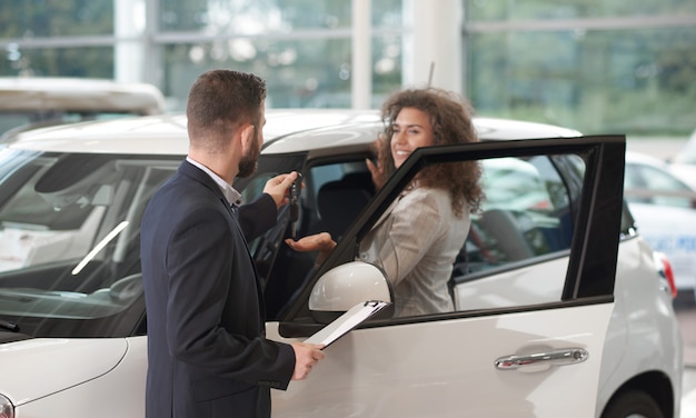 Glückliche Frau, die Schlüssel oh Neuwagen vom Manager nimmt.