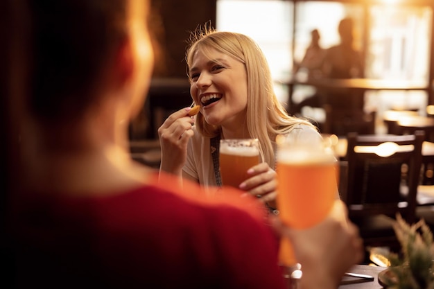 Glückliche Frau, die Spaß beim Essen und Trinken von Bier mit ihrer Freundin in einer Taverne hat