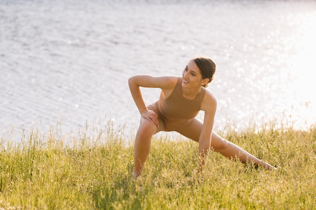 Glückliche Frau, die Yoga im Freien am Fluss praktiziert