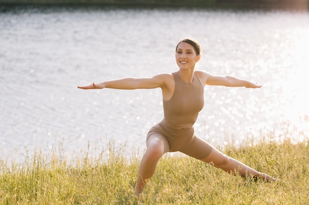 Glückliche Frau, die Yoga im Freien am Fluss praktiziert