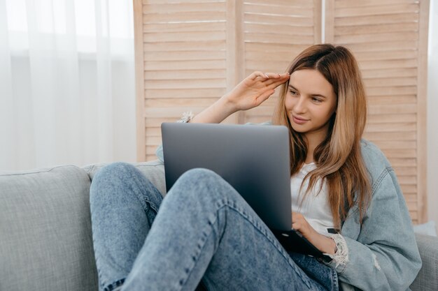 Glückliche Frau, die zu Hause auf dem Sofa liegt und auf den Computerbildschirm schaut und einen Videoanruf macht