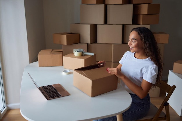 Glückliche Frau, die zu Hause Behälter auspackt und Karton öffnet, der in das Paket schaut Lächelnder zufriedener Kunde, der ein Paket vom Bestelllieferdienst erhält, der den Kauf auspackt