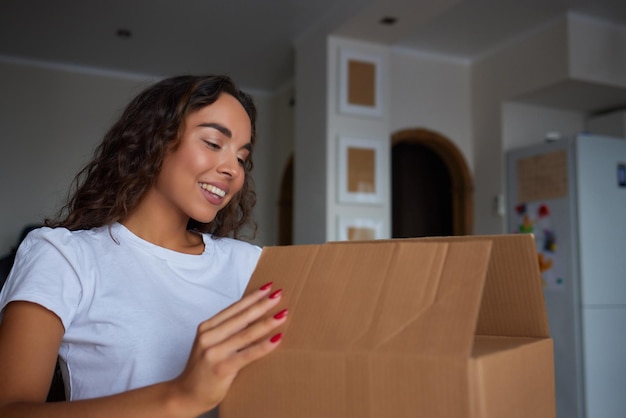 Glückliche Frau, die zu Hause Behälter auspackt und Karton öffnet, der in das Paket schaut Lächelnder zufriedener Kunde, der ein Paket vom Bestelllieferdienst erhält, der den Kauf auspackt