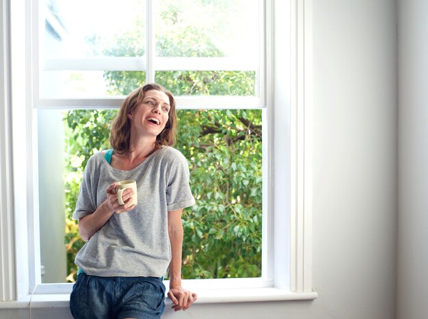 Glückliche Frau, die zu Hause mit einem Tasse Kaffee lacht