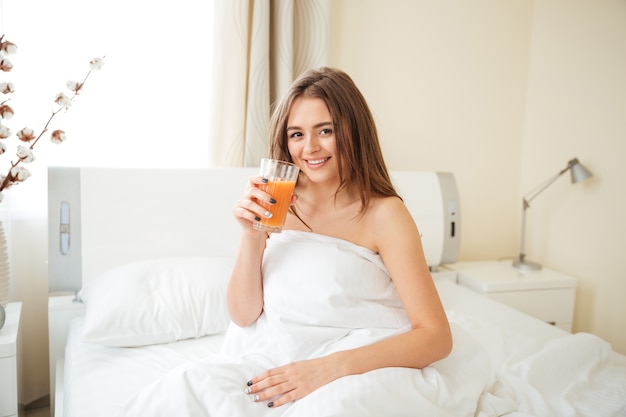 Glückliche Frau, die zu Hause Orangensaft auf dem Bett trinkt