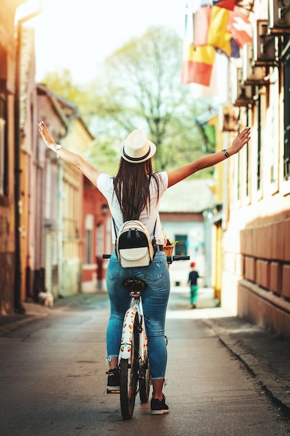 Glückliche Frau fährt mit dem Fahrrad entlang der Stadtstraße, an sonnigen Sommertagen, und genießt Aktivitäten im Freien.