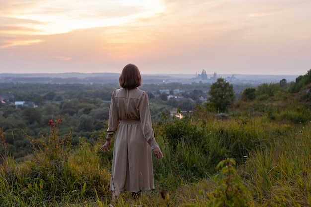 Glückliche Frau geht bei Sonnenuntergang auf einem Hügel mit Blick auf den Fluss