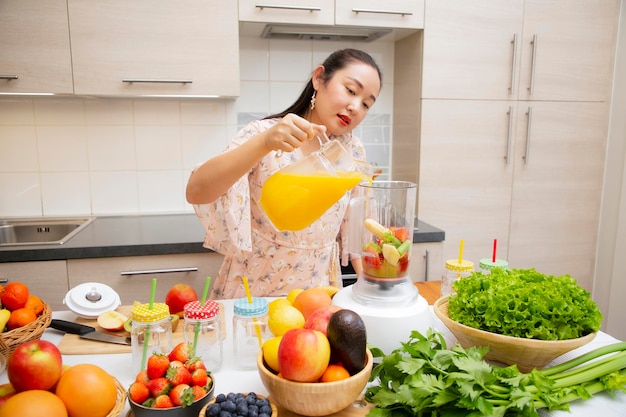 Glückliche Frau genießt es, frisch gepresste Früchte mit Gemüse zuzubereiten, um gemeinsam Smoothies zum Frühstück in der Küche zuzubereiten. Ernährungs- und Gesundheitskonzept.