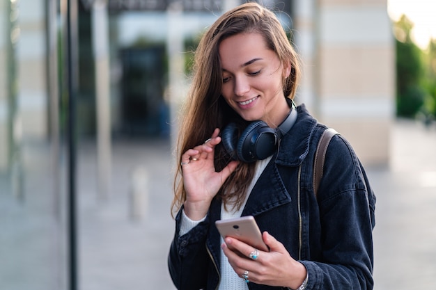Glückliche Frau genießt Musik in drahtlosen Kopfhörern, während sie durch die Stadt geht