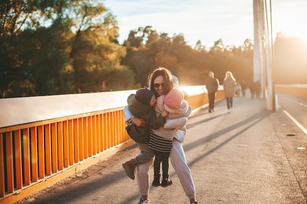 Glückliche Frau hält ihre beiden Kinder im Arm und vergnügt sich an einem sonnigen Herbsttag gemeinsam im Freien