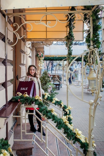 Glückliche Frau hält Papiertüten mit dem Symbol des Verkaufs in den Geschäften mit Verkäufen zu Weihnachten in der ganzen Stadt Konzept des Einkaufs Feiertage Glück Weihnachtsverkäufe