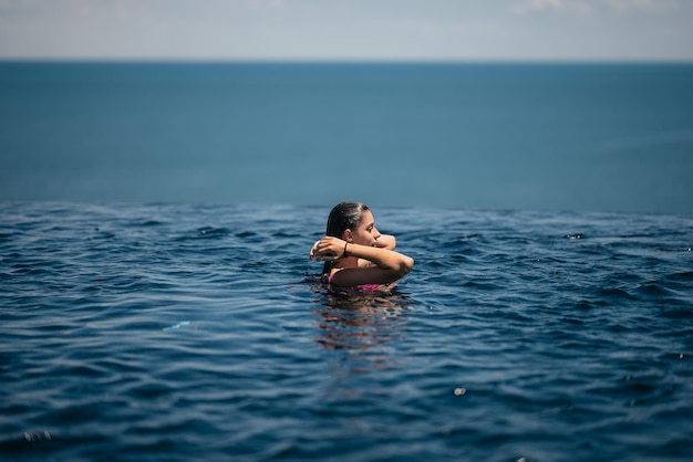 Glückliche Frau im Badeanzug schwimmt im Infinity-Pool am Meer