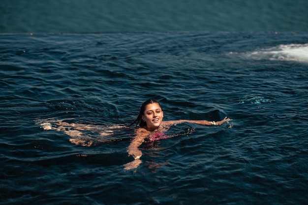 Glückliche Frau im Badeanzug schwimmt im Infinity-Pool am Meer