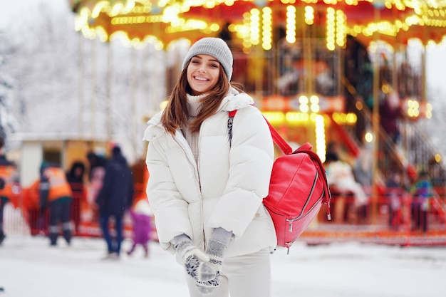 Glückliche Frau im weißen Mantel geht auf dem Weihnachtsmarkt spazieren, während sie Rucksack-Lifestyle-Ferien hält
